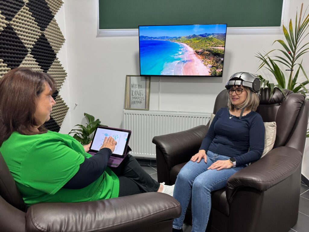 Eine Frau mit VR-Helm lächelt entspannt, während eine andere Frau in Grün ein Tablet benutzt